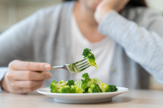 Close up of a woman hand holding fork with green broccoli over a white plate for healthy low calorie weight loss diet meal