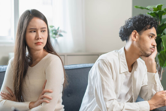Family problem concept. Tension in relationship between married couple, husband and wife staying sitting separate after quarrel in the living room.