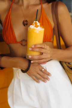 Mango Smoothie with Cream Topping Held by Woman in Orange Bikini Close