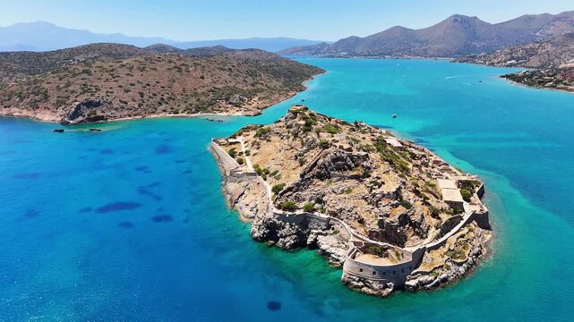 Spinalonga fortress occupies rocky Kalydon Island with Venetian walls, stone ruins and coastal paths surrounded by turquoise Mirabello Bay in the Cretan Sea, Lasithi, Crete, Greece, parallax orbit.
