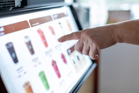 Selective focus to hand of customer with blurry touchscreen that using self service kiosk interactive touchscreen display to order drinks in coffee shop.