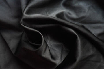 Fototapeta premium Black silk fabric with folds and twist creating flow and movement.