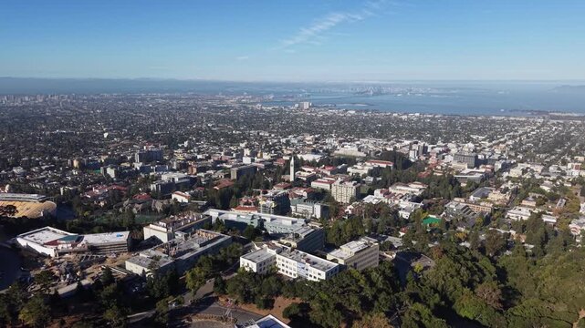 Daytime drone video sweeps over UC Berkeley campus, lush greenery, and downtown, revealing Bay Area skyline and San Francisco Bay in crisp, vibrant aerial footage.