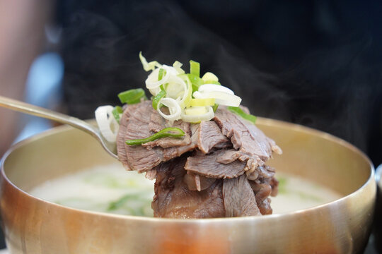 Spoonful of tender sliced beef brisket from a steaming hot traditional Korean bone broth soup seolleongtang served in a brass bowl