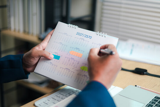Businessman writing on a calendar while planning dates, appointments, deadlines and annual schedule at a desk with laptop, representing time management