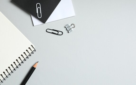 Notebook with pencil and office supplies on grey background, top view
