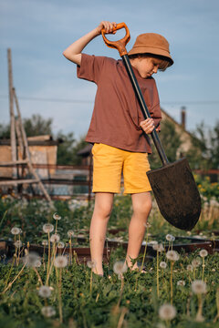 Young boy with a shovel standing barefoot in a garden