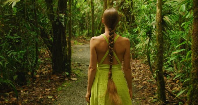 Woman with long braid walking down narrow path in dense tropical jungle Costa Rica