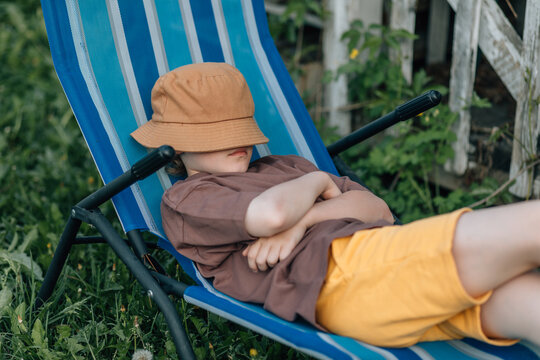 Child sleeping outdoors in a striped lounge chair