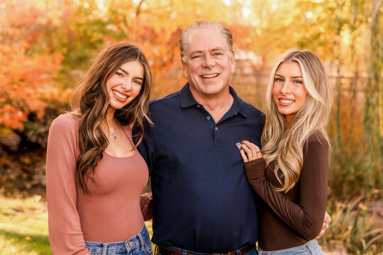 Happy father posing with his two adult daughters outdoors in autumn