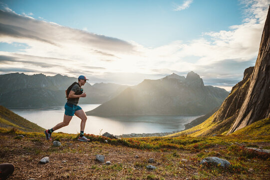 Man trail running on mountain ridge overlooking a fjord