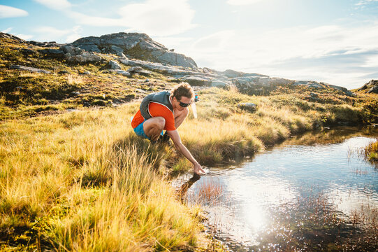 Trail runner refills water in a sunny mountain pond