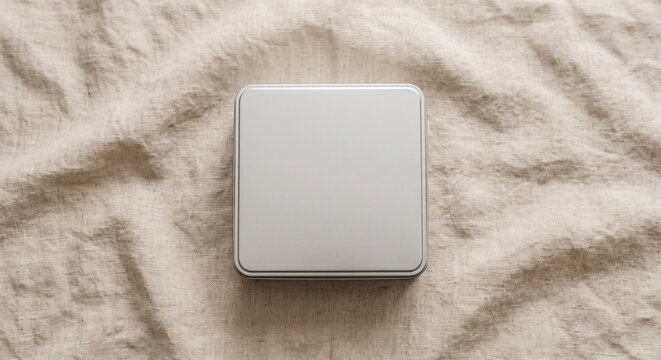 Square metal tin box with lid on a wrinkled beige linen fabric cloth in top view flat lay for mockup design