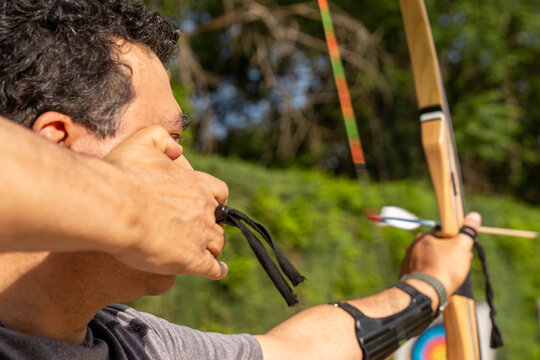 Archer concentrating, drawing bowstring, and aiming arrow towards target during practice