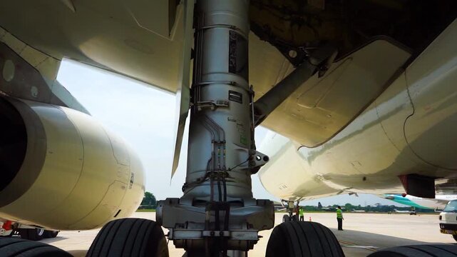 Low angle view of massive commercial aircraft main landing gear strut and turbofan engine housing parked on airport apron during pre flight maintenance inspection