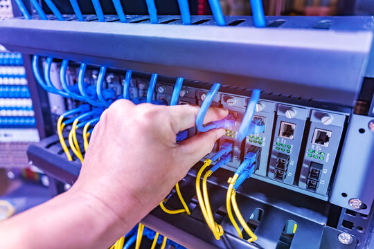 hand with Fiber Optic cables connected to an optic ports and Network cables connected to ethernet ports and UTP Network in a datacenter