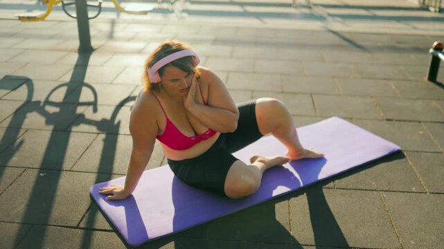 Tired obese female sitting on a fitness mat recovering after a morning workout.