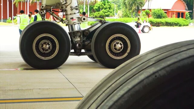 Detailed view of commercial airplane main landing gear assembly with dual heavy duty rubber tires and hydraulic shock strut parked on airport tarmac apron during pre flight maintenance service