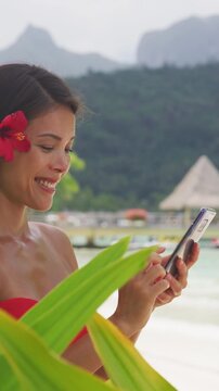 Asian beauty woman using phone in bikini on tropical beach. Beautiful young woman on vacation and travel using smartphone app. Raw unedited vertical video of real woman model without any makeup