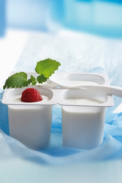 Four open yoghurt cups with fruit and mint leaf, close-up