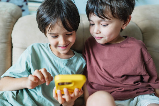Two brothers play a game on a yellow smartphone at home