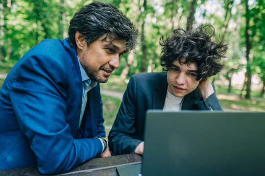Mature man and teenage boy use a laptop outdoors