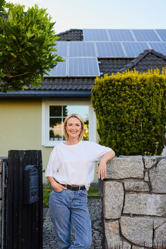 Woman standing by fence in front of house with solar panels