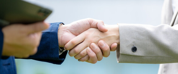 Business partnership concept with professional colleagues shaking hands while holding tablet outdoors in urban setting. partnership, business, handshake, agreement, professional. © eakgrungenerd