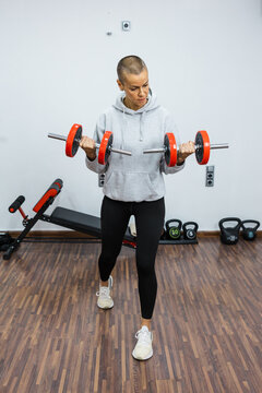 Determined sportswoman lifting dumbbells, exercising biceps in gym