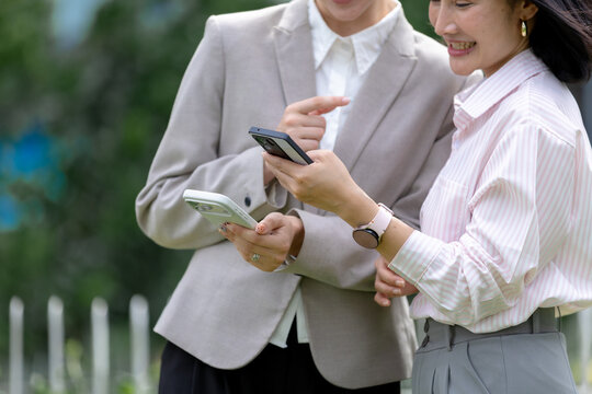 Mobile communication concept with two businesswomen smiling and using smartphones together outdoors in business district. smartphone, business, women, communication, technology.