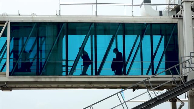Low Angle Shot Of Passengers Walking Through Airport Jet Bridge Boarding Passageway Glass Aerobridge Tunnel Silhouette Travelers Flight Departure Transit Commercial Aviation Transport Concept
