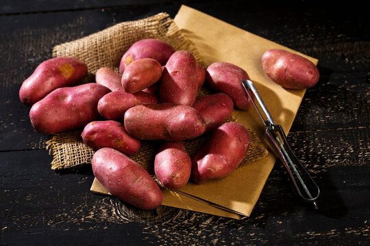 Raw Grenaille potatoes and peeler on brown paper, jute and dark wood