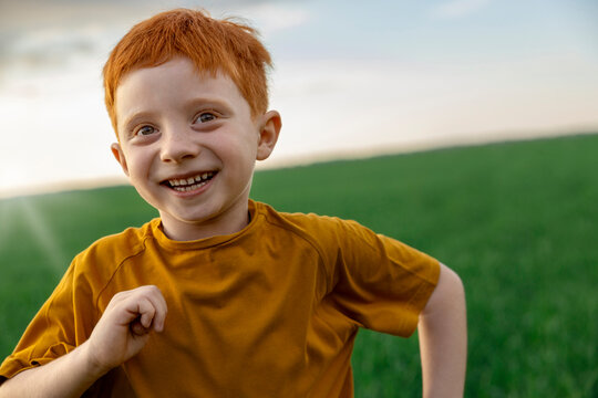 Cheerful boy with red hair runs across a green field