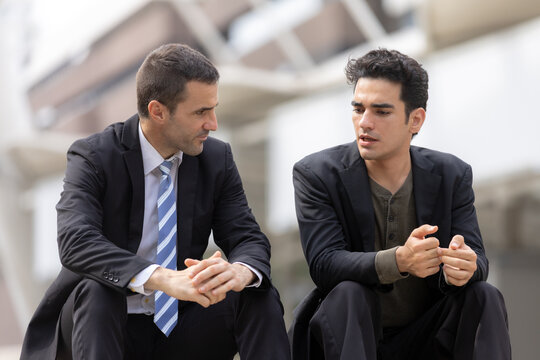 Business mentoring concept with two professional men having focused conversation while sitting outdoors in corporate area. mentoring, business, discussion, professional, colleagues.