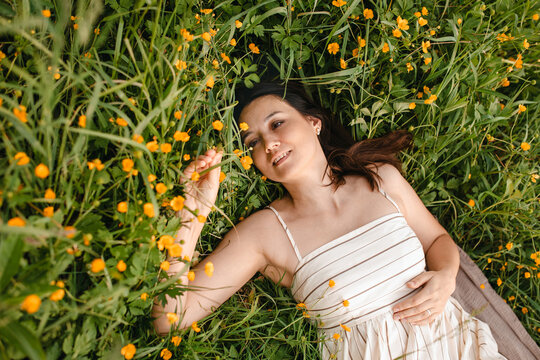 Mature woman relaxes in a summer meadow with yellow wildflowers