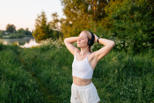 Woman in sportswear enjoys music and relaxation outdoors at sunset