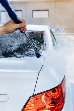 Man washes a white car with a high pressure water jet