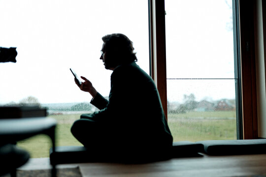 A silhouetted businessman uses a smartphone by the window