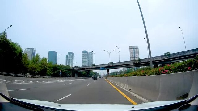 Driving car dashcam perspective on urban highway passing under concrete overpass bridge structures with modern high rise skyscrapers in background transportation and infrastructure concept