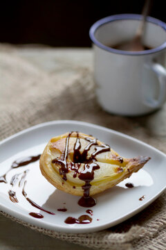 Pear in puff pastry on plate with mug of chocolate sauce, close up