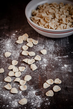 Orecchiette in a bowl and on wooden table with flour