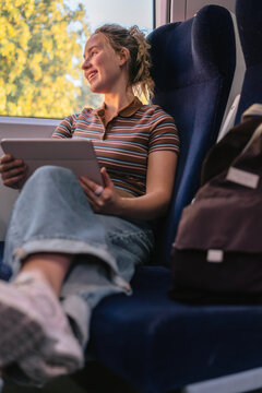 Smiling woman looks out the train window holding a tablet