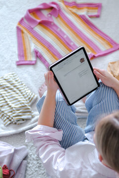 Woman sits indoors holding tablet for sustainable clothing resale