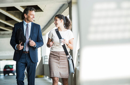 Mature businessman and young colleague walking in parking garage, talking