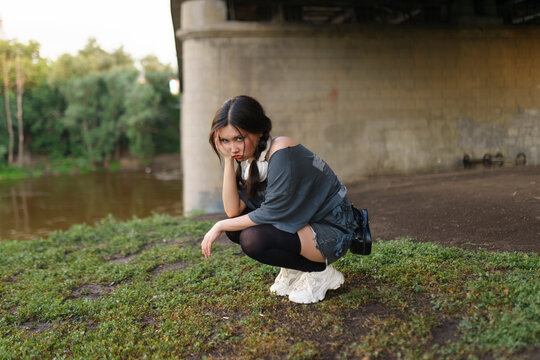 Young woman squats under a city bridge during a summer evening