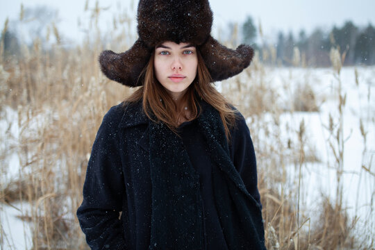 Winter portrait of woman with fur ushanka in snowy field outdoors