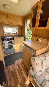 Compact caravan kitchen interior with wooden cabinetry, gas stove, refrigerator and counter space