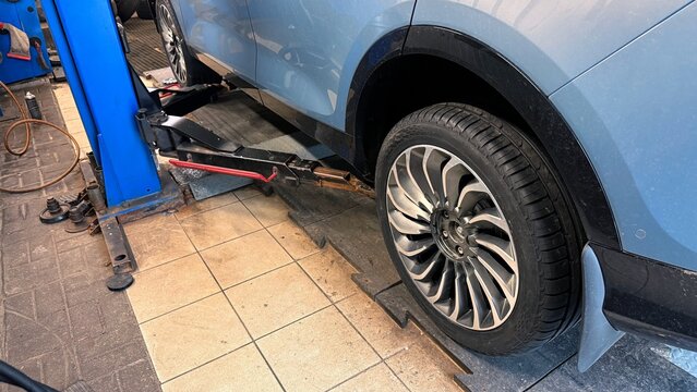 Car tire on a hydraulic lift showcasing detailed wheel rim and winter summer tread patterns closeup