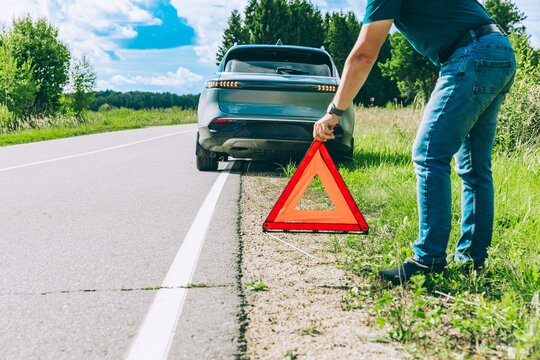 Person setting up an emergency warning triangle near a broken electric hybrid car on roadside