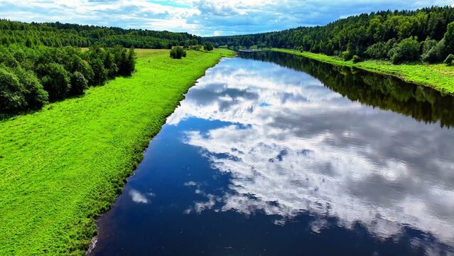 River reflecting cloudy sky surrounded by lush greenery and trees in late spring season